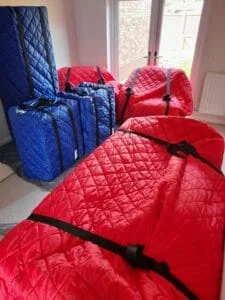 Furniture wrapped in red and blue quilted protective covers with straps for moving