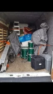 Moving van loaded with drums, bicycle, ladders, and covered household items