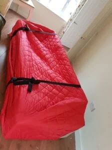 Sofa wrapped in red quilted protective moving cover with black securing straps