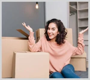Smiling woman sitting among moving boxes in new home