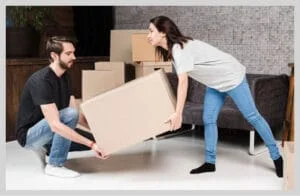 Couple lifting a cardboard box together during home move with packed boxes in the background