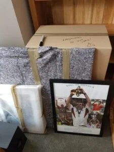 Packed moving box labeled fragile with bubble-wrapped and blanket-wrapped items, plus framed sports photo